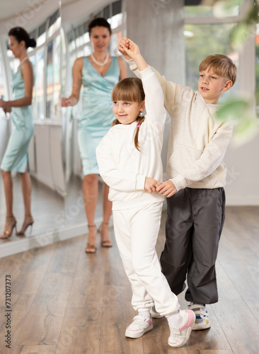 Passionate tween dancers, girl and boy practicing ballroom dancing in dance studio, gracefully performing waltz while female trainer monitoring technique and progress..