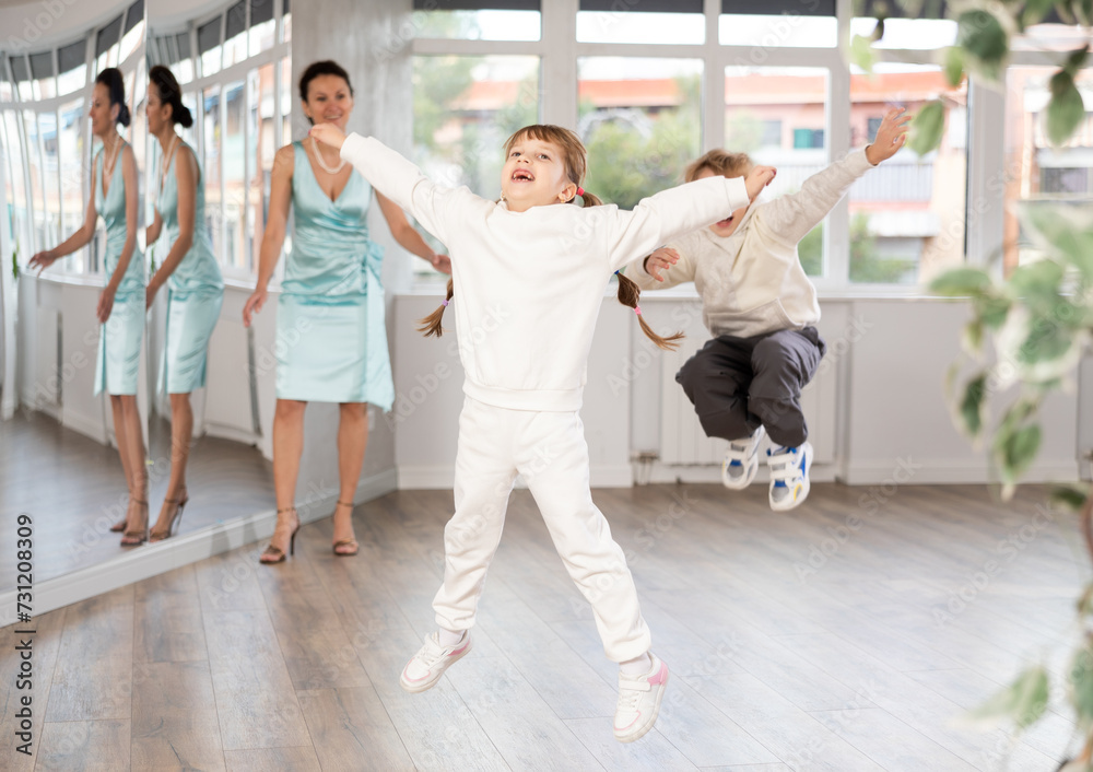 Fototapeta premium Cheerful preteen girl captured in air while jumping during lively dance lesson with boy classmate and female teacher in background in choreography studio..