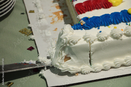 birthday anniversay wedding celebration even cake cut with knife sliding under piece, white blue red and yellow photo