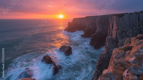 The sun dips below the horizon, illuminating the ocean cliffs with a fiery glow against the evening sky.