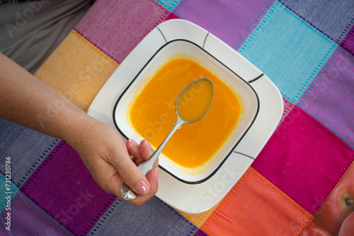 Hand with spoon on a plate with carrot soup