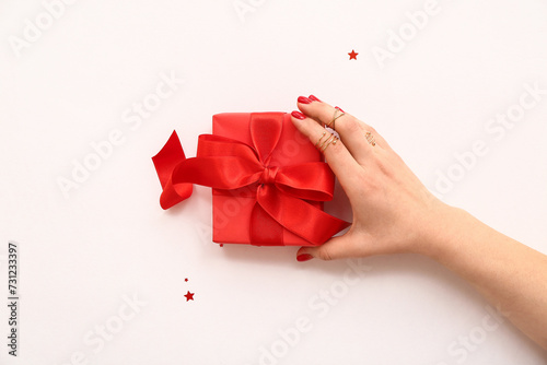 Fototapeta Naklejka Na Ścianę i Meble -  Female hand with stylish red manicure holding gift box on white background