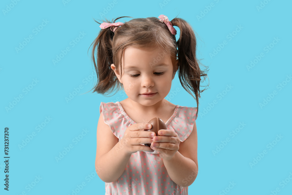 Happy cute little girl eating tasty chocolate egg on blue background Happy cute little girl eating tasty chocolate egg on blue background