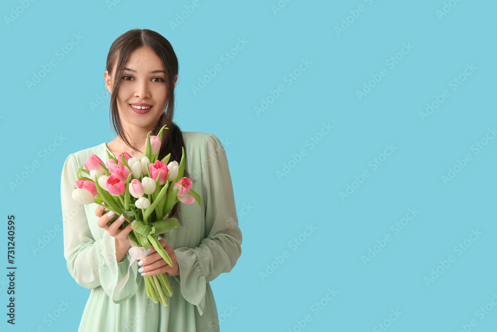 Pretty young Asian woman with bouquet of beautiful tulips on blue background. International Women's Day