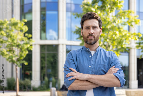 Confident businessman in casual attire standing arms crossed outside modern office
