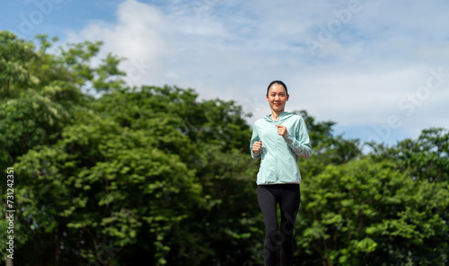 Happy asian slim woman wearing sportswear jogging on track at sport stadium. Young beautiful asian female in sports bra running outdoor. Workout exercise in the morning. Healthy and active lifestyle