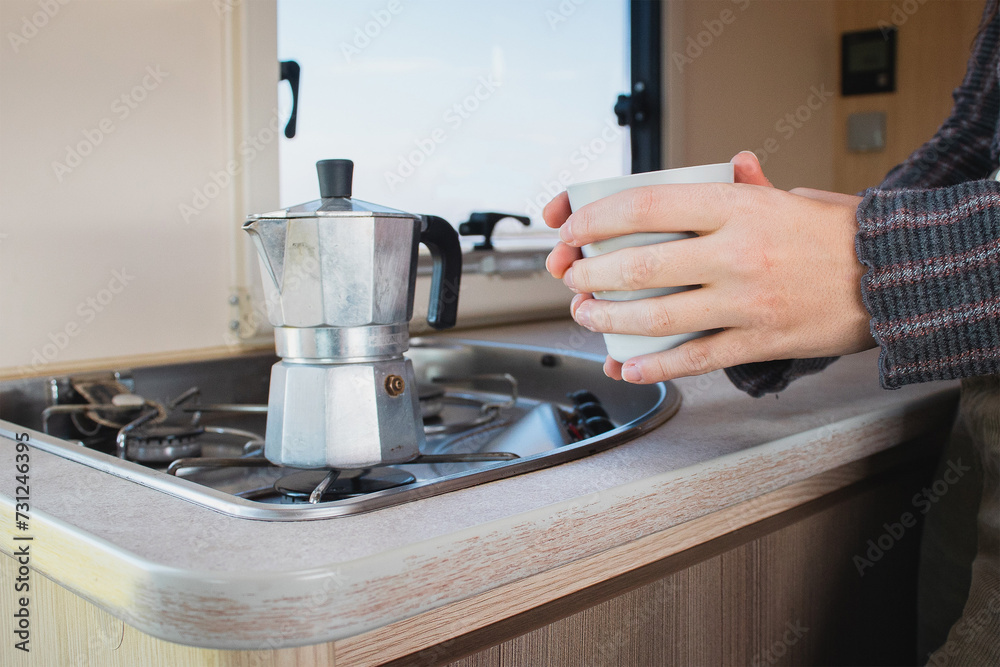 hands hold a glass next to a coffee pot in a coach kitchen.
