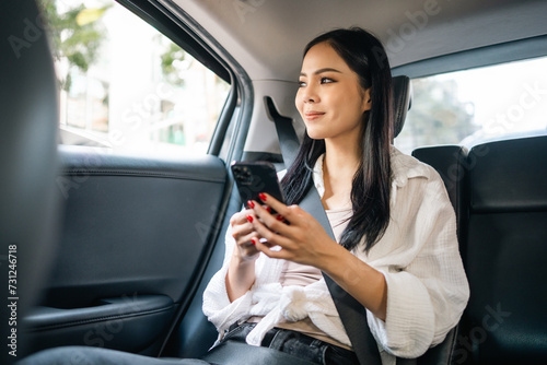 Asian Woman Traveler sitting in car back seats using smartphone call taxi service in application. Online app with cell phone and put on safety belt. Female passenger in car traveling to destination. © Chanakon