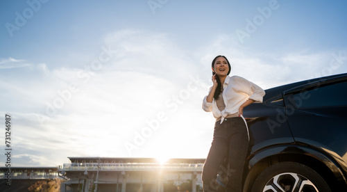 Young beautiful asian women buying new car. she was standing near car on the roadside. Beautiful moment blue sky Smiling female driving travel by vehicle on the road on a bright day with sun light.