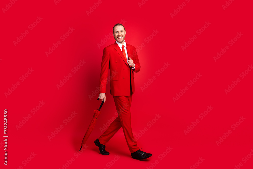 Full length photo of elegant young male walking outside umbrella dressed stylish classic garment isolated on red color background Full length photo of elegant young male walking outside umbrella dressed stylish classic garment isolated on red color background