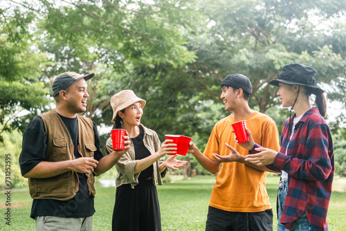 Cheers! Group of asian people friend party camping in nature making toasting with soft drink and beer red cup. Hangout party outdoor in campsite nature forest background on holiday weekend vacation photo