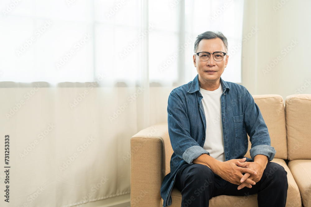 Handsome asian mature old man sitting on sofa couch in living room at home. Happy Portrait of cheerful smiling senior asian man relax in the house. Mature People and lifestyle Handsome asian mature old man sitting on sofa couch in living room at home. Happy Portrait of cheerful smiling senior asian man relax in the house. Mature People and lifestyle
