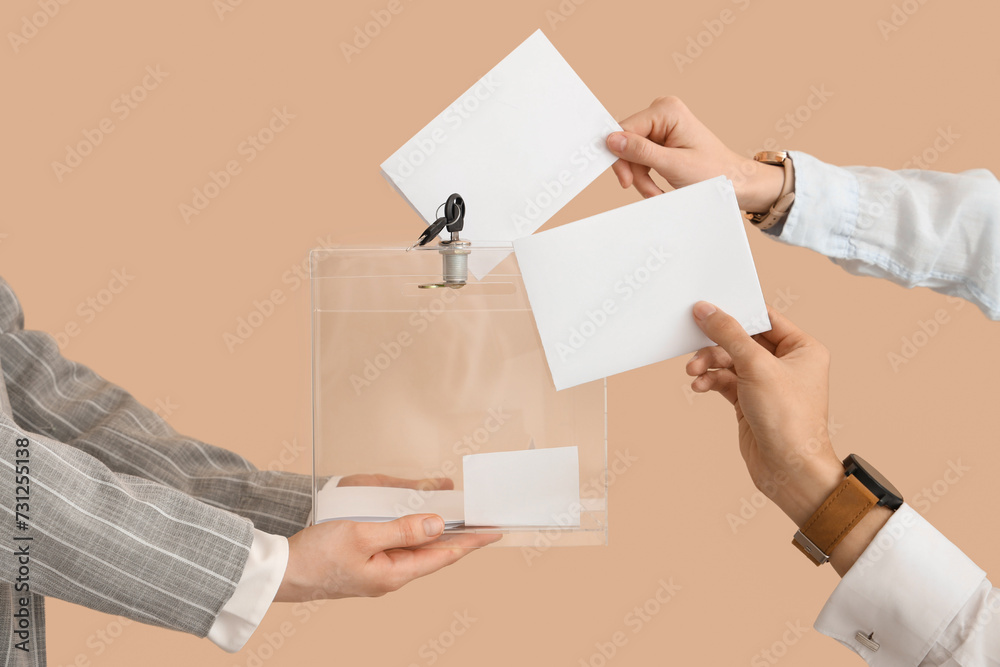Fototapeta premium Hands putting voting paper into ballot box on beige background. Election concept