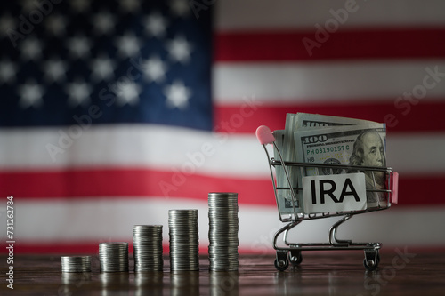 Money towers and shopping cart used for saving US dollar bills and notes for IRA retirement fund on the American flag background, closeup. Finance, business, investment and money saving concept