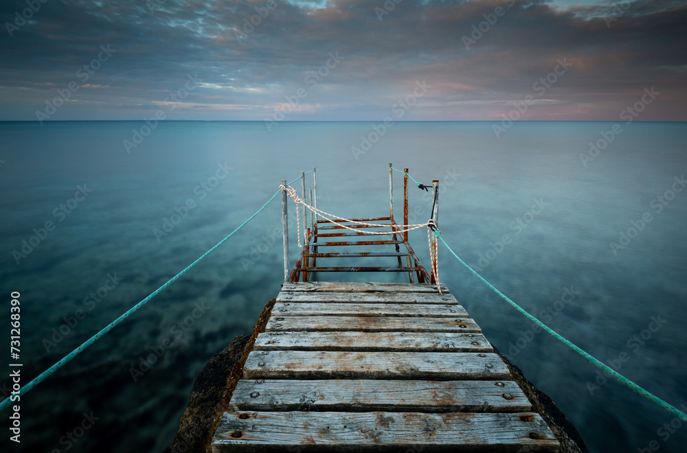 Obraz premium Long wooden pier in the sea at sunset.