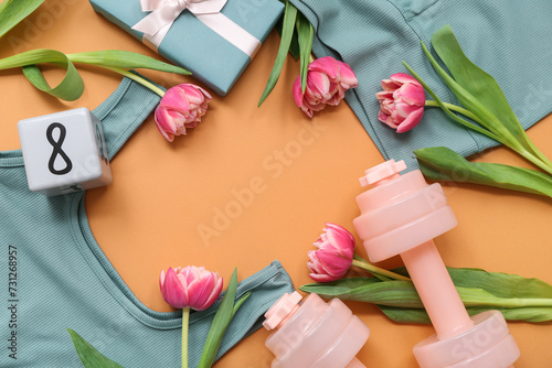 Frame made of sports clothes, dumbbells, gift and tulip flowers on color background