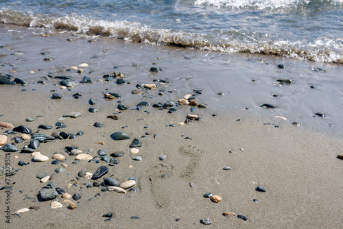 Sea beach with two footprints on the sand among stones and pebbles