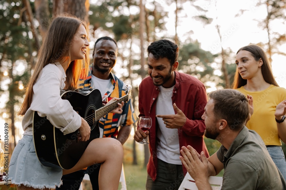Obraz premium Attractive hipster woman playing guitar winning over men at dinner party with multiracial friends