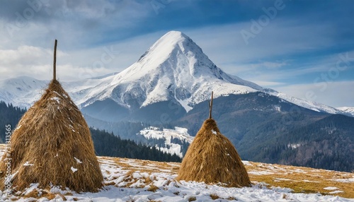 snowy mountain peak at carpathian mountains pair of haystacks on foreground ukraine photo