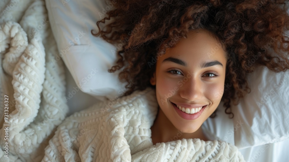An overhead view of a smiling woman lying in bed, covered with a white color blanket An overhead view of a smiling woman lying in bed, covered with a white color blanket