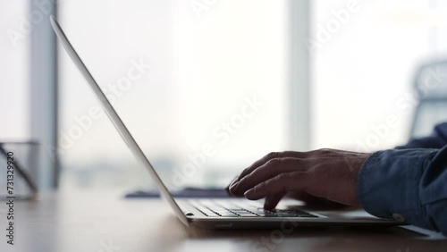 Side view. Silhouette. Close up of male hands typing on a laptop keyboard. Businessman or IT programmer uses a computer while sitting at a desk at a workplace in a business office. Man fingers texting photo