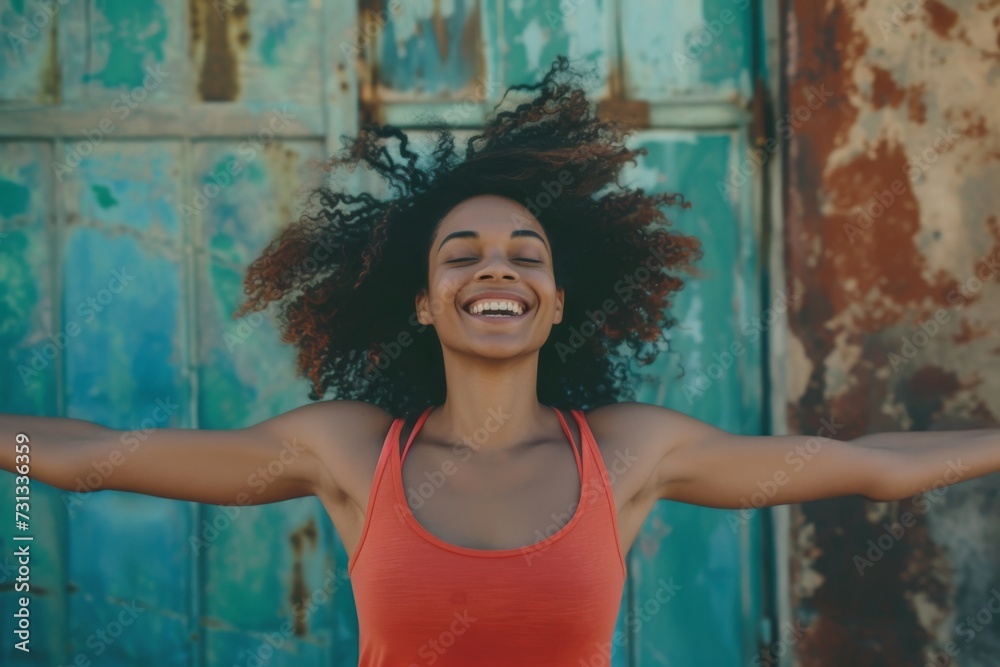 Fototapeta premium A carefree woman stands against a vibrant wall, her curly hair framing her closed eyes as she smiles in contentment