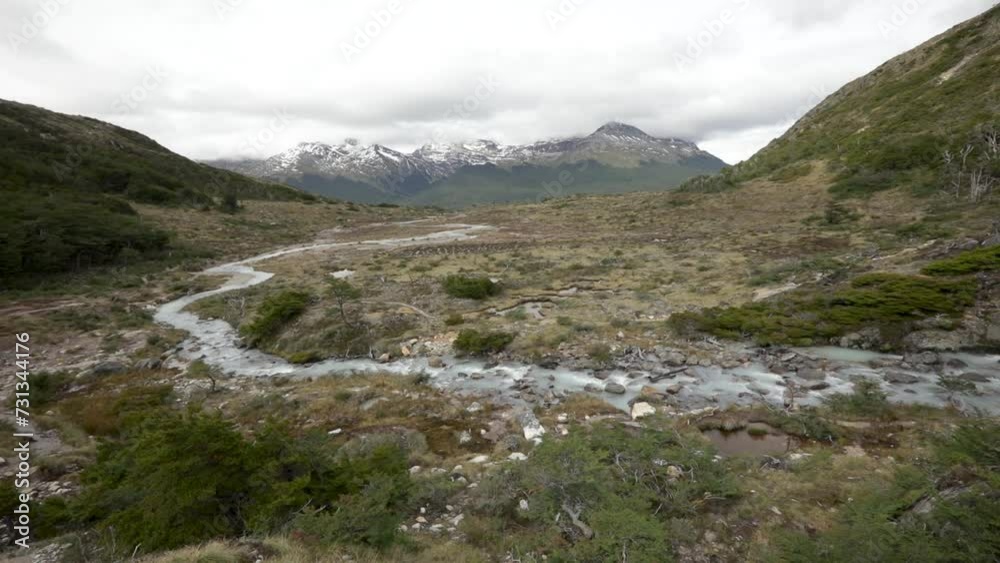 Alpine landscape in autumn. Panorama view of the glacier water stream flowing downhill across the yellow grassland, Andes mountains and forest in Ushuaia, Tierra del Fuego, Patagonia Argentina. Alpine landscape in autumn. Panorama view of the glacier water stream flowing downhill across the yellow grassland, Andes mountains and forest in Ushuaia, Tierra del Fuego, Patagonia Argentina.