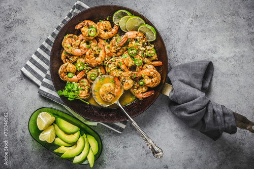 Shrimp with Chili, Lime and coriander in butter sauce, carbon steel skillet, with sliced avocado on gray linen napkins and silver spoon photo
