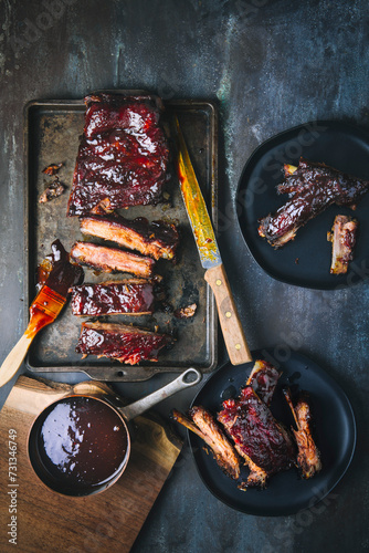 Glazed barbecued pork ribs, sliced and whole, on tray and two serving plates, with pot of sauce and meat knife photo