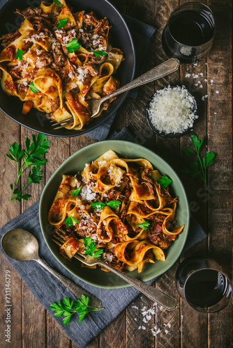 Medium shot of two bowls (green and black) of fresh pasta noodles with meat and tomato ragu with forks, parsley, red wine and grated cheese photo