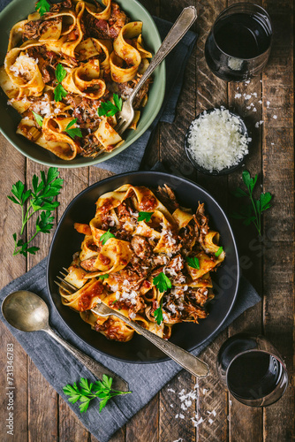 Medium shot of two bowls (black and green) of fresh pasta noodles with meat and tomato ragu with forks, parsley, red wine and grated cheese photo