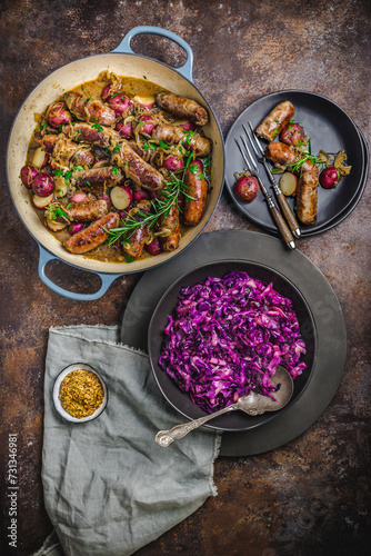 Dutch oven with sausages, potatoes, herbs, with bowl of bright red cabbage photo