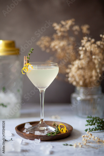 A vodka amd lemon cocktail served in a Nick and Nora glass and garnished with a lemon zest spiral and fresh thyme. photo