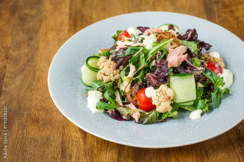 Salmon salad with mixed vegetables on a plate on wooden table in a restaurant Salmon salad with mixed vegetables on a plate on wooden table in a restaurant