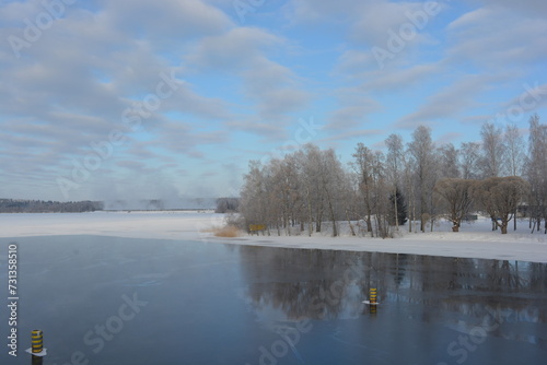 A real snowy Finnish winter with lakes in Varkaus, Finland. A clear lake with beautiful clouds, light blue sky, trees, birches, fir trees, spruces growing in wildlife.