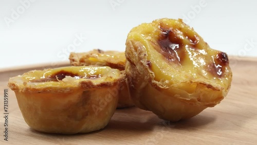 Three traditional Portuguese desserts Pastel de Nata or Pastel de Belem. Egg custard tart sprinkled with cinnamon. Rotating popular Portuguese pie with golden brown crust on a wooden background.