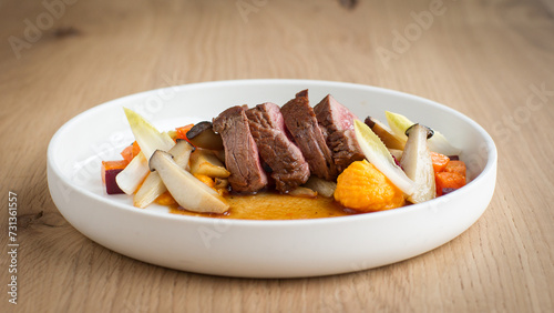 Slices of steak with mixed seasonal vegetables, mushrooms and gravy on a white plate on a wooden background