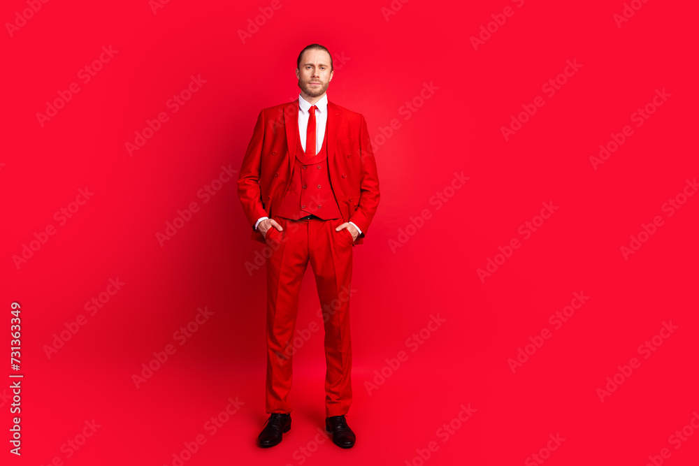 Full length photo of elegant young male hands pockets posing defile dressed stylish classic garment isolated on red color background Full length photo of elegant young male hands pockets posing defile dressed stylish classic garment isolated on red color background