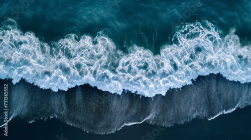 Aerial drone view or top view perspective photography of a beautiful transparent clear sea or ocean waves and foam splashing on the dark navvy blue or gray sand beach 
