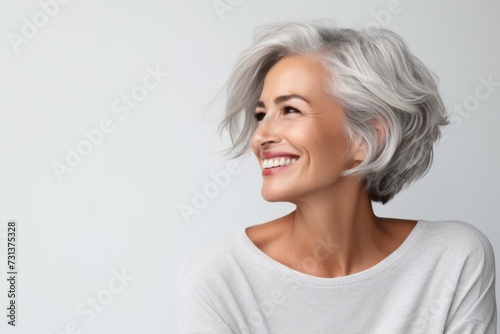 Portrait of a beautiful middle aged woman with grey hair smiling against grey background