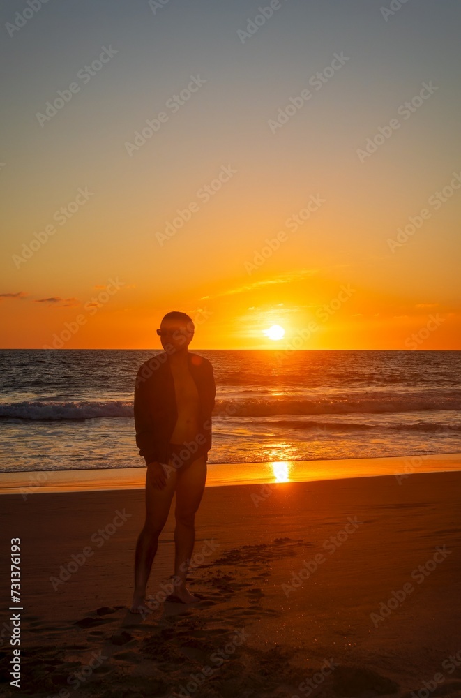 Young man standing on the beach enjoying sunny sunset at the seashore
