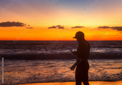 Man checking phone while enjoying beautiful sunset walking on the beach