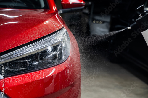A man washes the headlights of a red car with a spray.  © Михаил Решетников