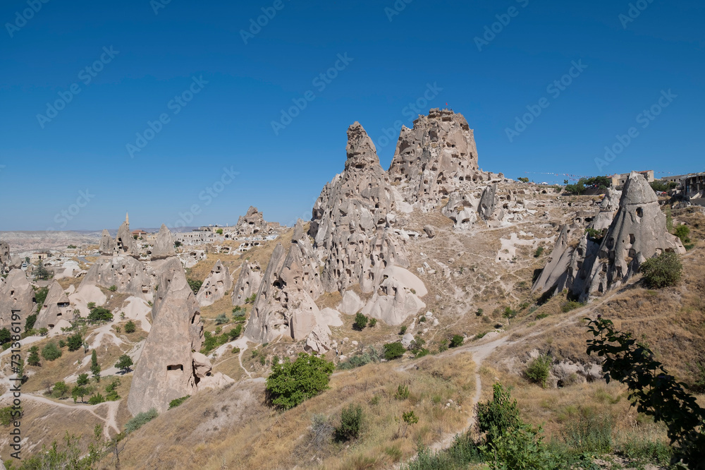 general view of the cave village of Uchisar in Cappadocia with its castle carved out of volcanic rock against a blue sky, horizontal
