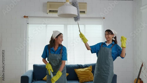 In messy living room two women in uniforms work cleaning employees. With gloves on they tackle dust and dirt on furniture sofas and floors. routine is house care and hygiene. agency small business photo