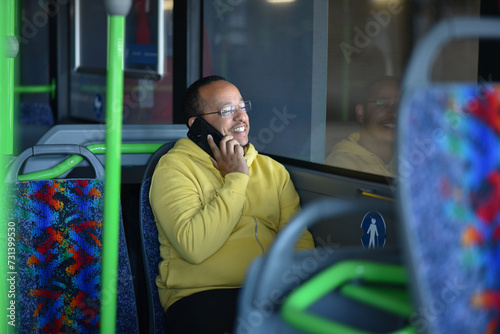 a lustful dark-skinned young man is sitting in the bus and talking on the phone photo