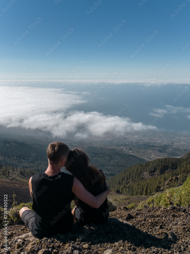 romantic lovely couple sitting on mountain top above clouds and looking on view