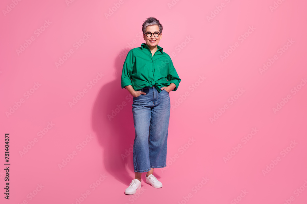 Fototapeta premium Full body photo of attractive pensioner woman posing hands pockets defile dressed stylish green clothes isolated on pink color background