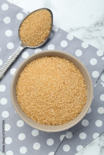 Brown sugar in bowl and spoon on white marble table, top view