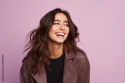 Happy young brunette woman in brown leather jacket over purple background.